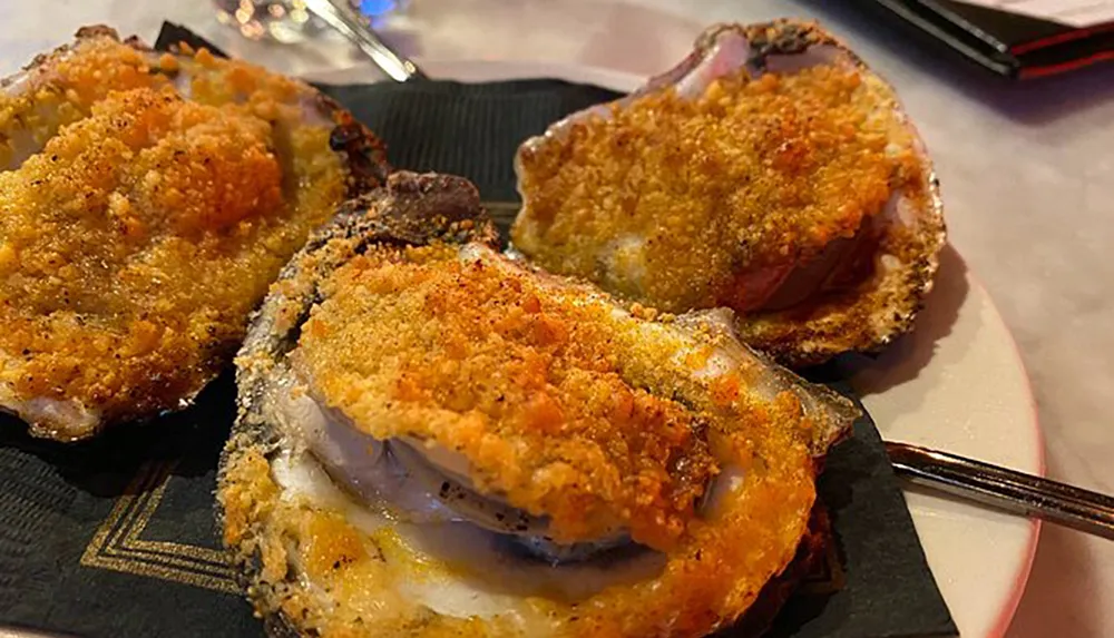 The image shows three golden-brown breaded oysters on the half shell presented on a dark plate with a fork in the background suggesting a ready-to-eat seafood dish