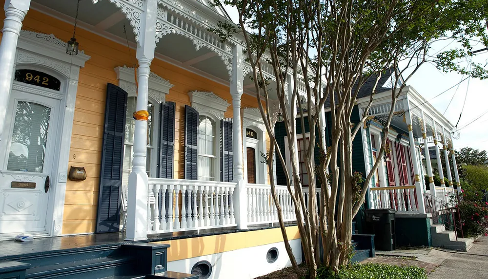 The image shows a picturesque street view of traditional houses with intricate woodwork and colorful facades typical of New Orleans architectural style