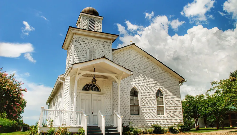 A quaint white church with decorative fish-scale shingles under a blue sky with white clouds