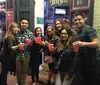 A group of people is posing for a photo on a street with drinks in hand smiling and looking at the camera