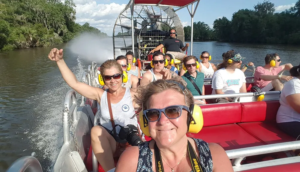Passengers are enjoying a sunny airboat tour with several wearing ear protection possibly indicating the high noise levels of the boat engine