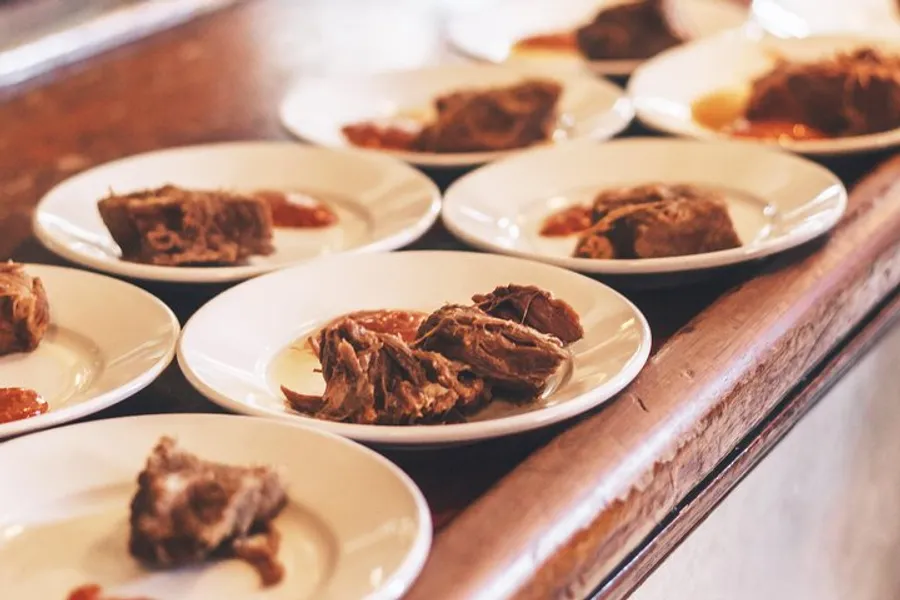 The image shows a series of white plates with portions of pulled pork, neatly arranged on a wooden counter.