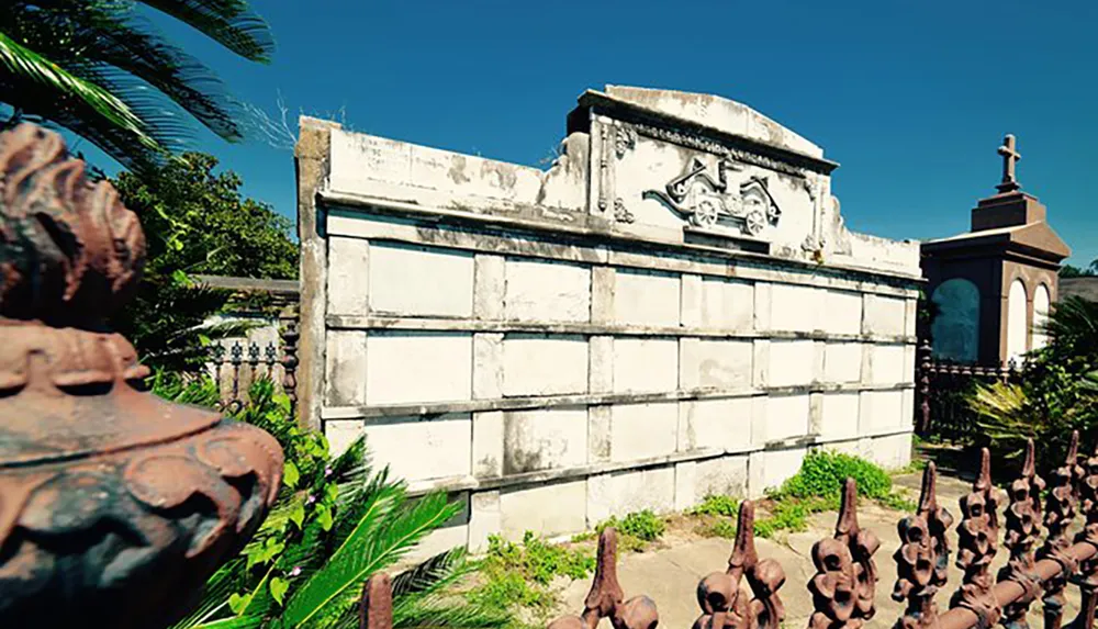 This image shows an ornate weathered crypt with rusting ironwork in a cemetery under a clear blue sky