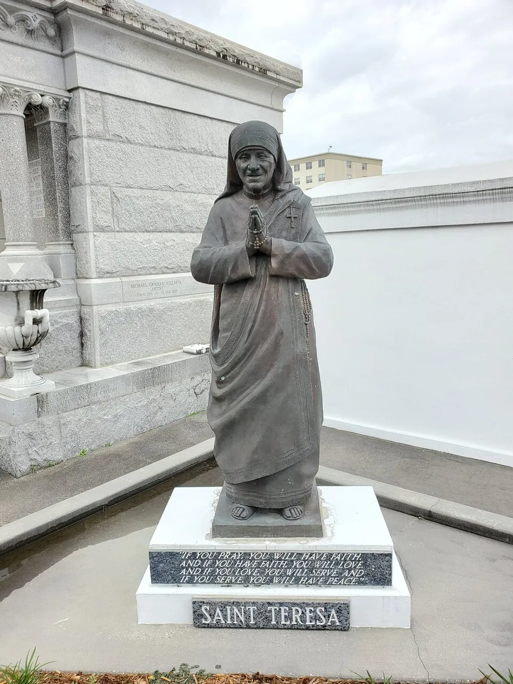 The image shows a statue of Saint Teresa represented in prayerful pose with an inscription at the base that offers a reflective quote on the virtues of prayer faith love and service