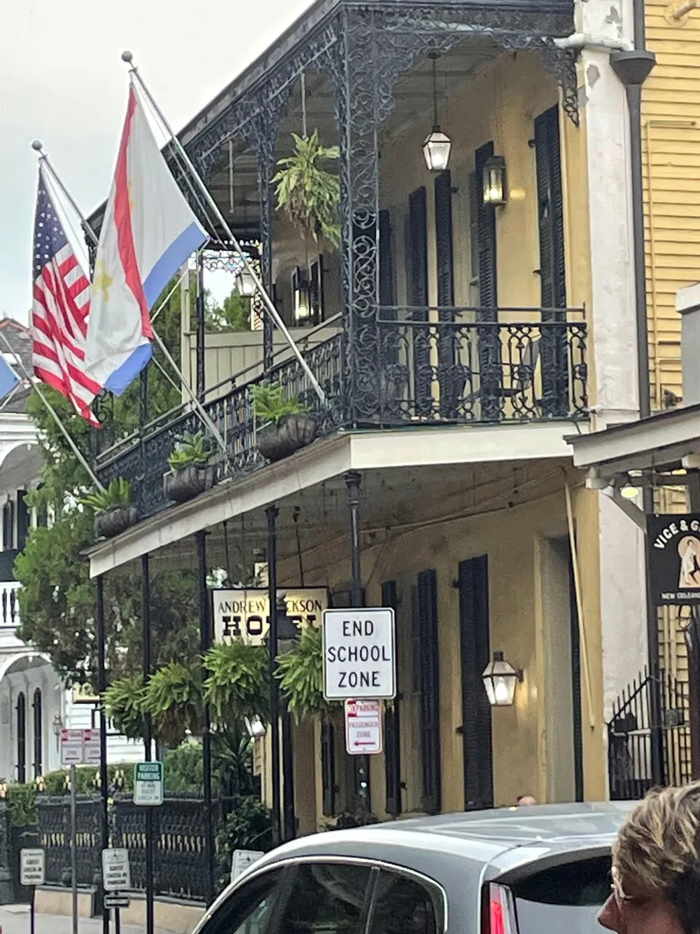 The image shows an ornate balcony on a historic building flying American and other flags with a street sign in front reading END SCHOOL ZONE indicative of the area likely being near a school
