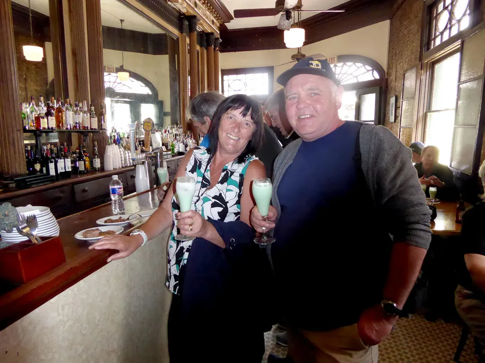 A couple is smiling while holding drinks at a bar with a classic decor