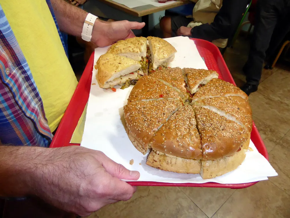 A person is holding a tray with a very large sliced sandwich filled with various ingredients