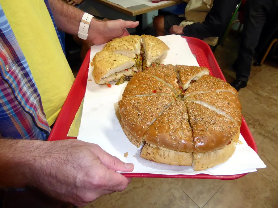 A person is holding a tray with a very large, sliced sandwich filled with various ingredients.