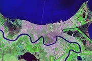 This image depicts an area with a prominent winding river cutting through a patchwork landscape of urban development and green spaces, presented in enhanced, unnatural colors likely indicating a satellite or infrared view.
