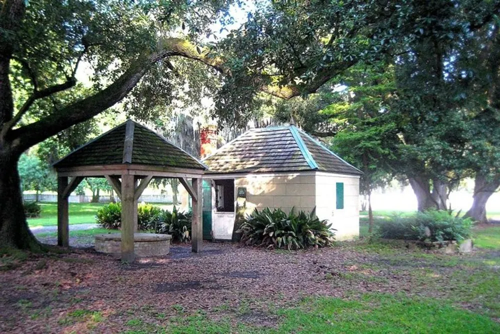 A small building with a green door is accompanied by a gazebo-like structure amidst a tranquil park with lush trees and sunlight filtering through the foliage