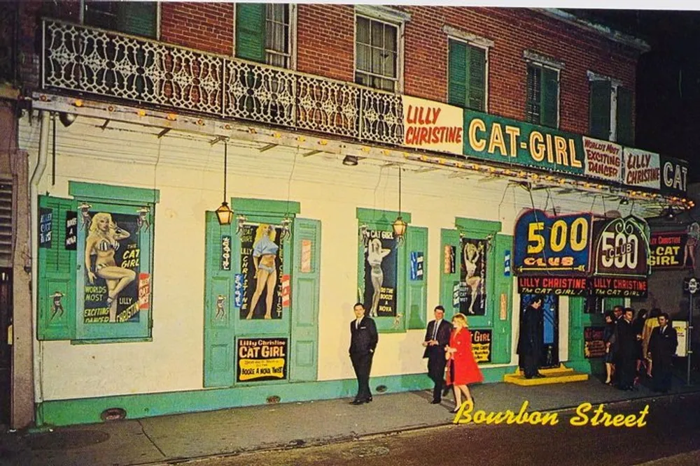 The image shows a lively vintage night scene on Bourbon Street with pedestrians walking past the colorful faade of the 500 Club featuring posters of the entertainer Lilly Christine the Cat Girl
