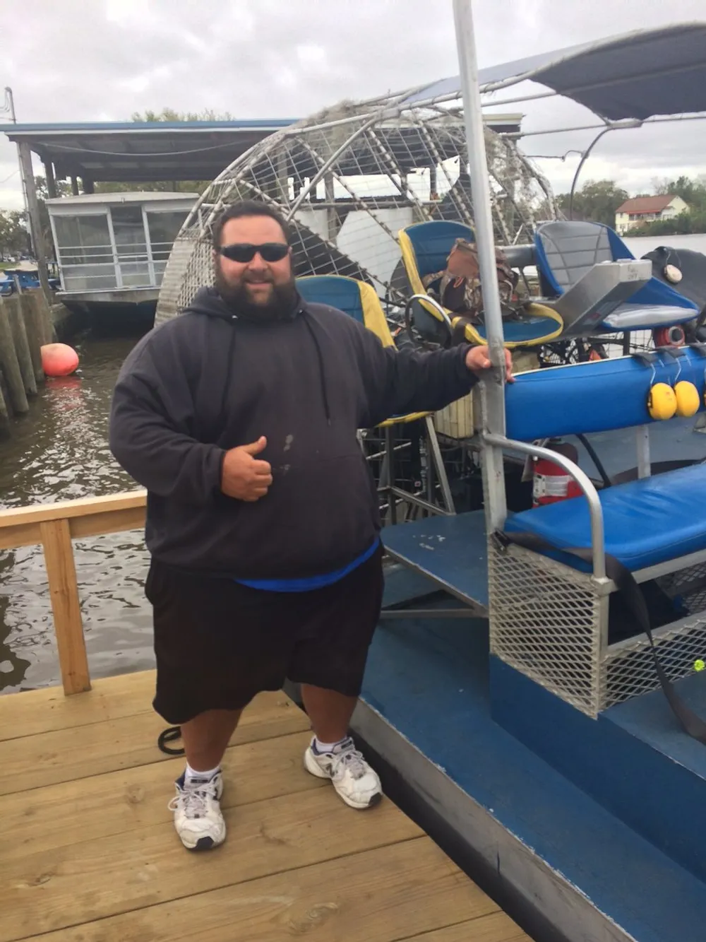 A person is giving a thumbs-up while standing next to an airboat at a dock