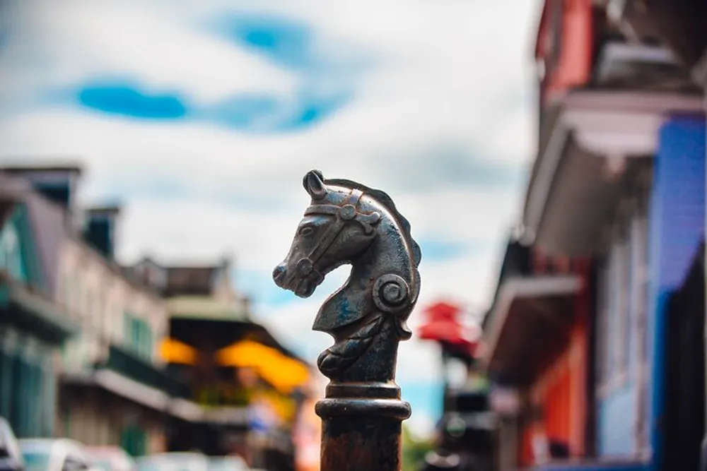 The image features a close-up of a metal horse head sculpture atop a post with a blurred urban street scene in the background