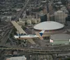 A small airplane is flying over an urban landscape with a distinctive domed stadium and intersecting highways