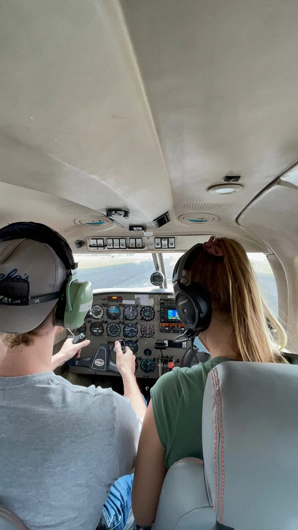 Two people wearing headphones are in the cockpit of a small aircraft with one of them handling the controls