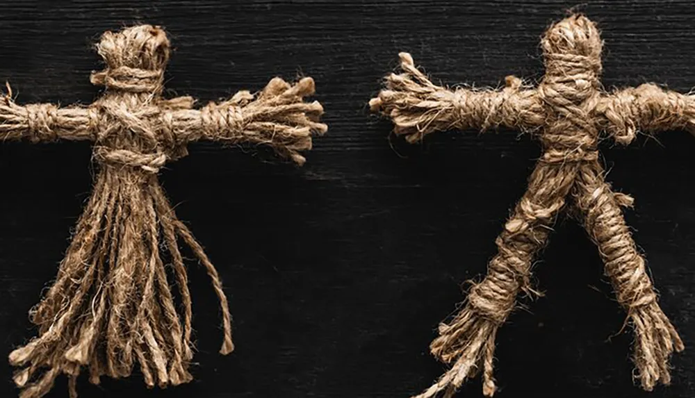 Two rustic figures made of twine resembling human shapes are positioned side by side against a dark wooden background