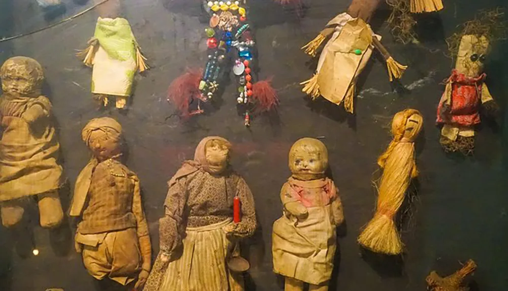 The image shows an assortment of old worn dolls of various sizes and styles displayed together some with missing parts or accessories