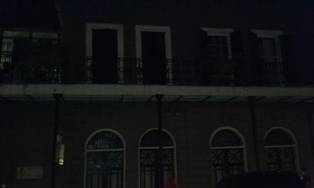 This is a poorly lit nocturnal photograph showing the facade of a building with a balcony and arched windows and a person on the sidewalk is visible on the right side of the image