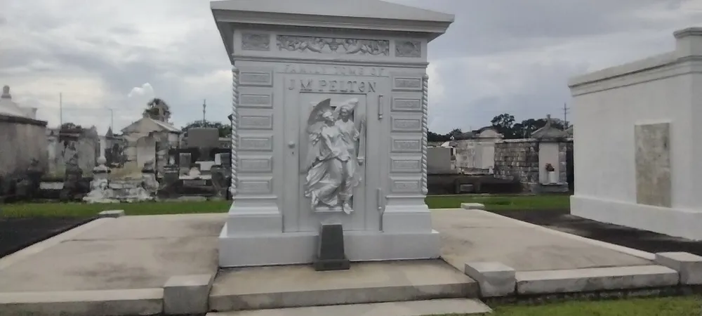 This image shows an ornate mausoleum with a sculptural relief on the door set amidst other burial structures in a cemetery under an overcast sky