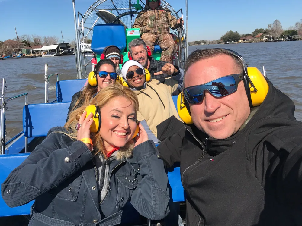 A group of happy people wearing protective earmuffs is taking a selfie on an airboat