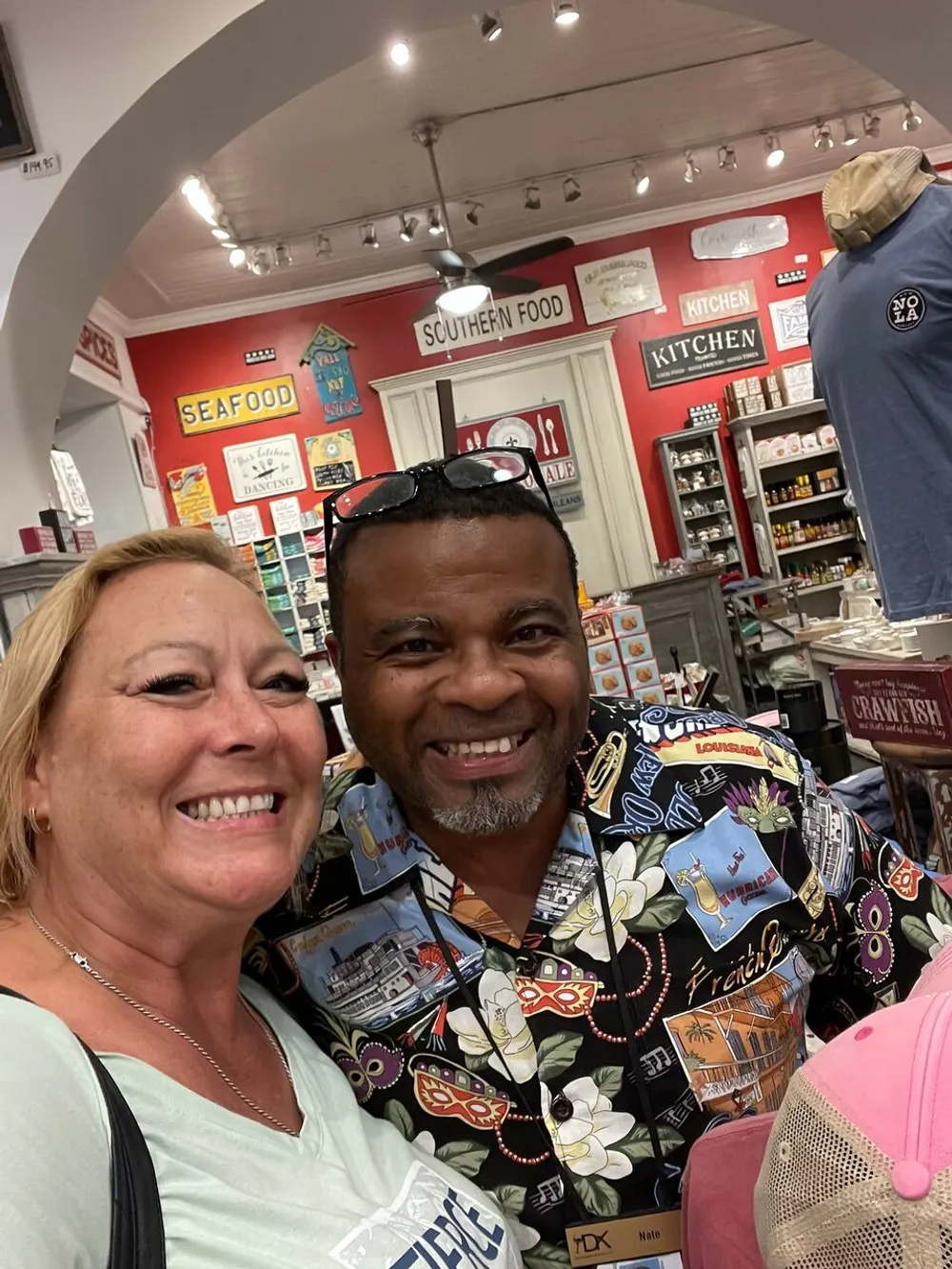 A man and a woman are smiling for a selfie inside a store with colorful dcor and merchandise that suggests a theme related to Southern or New Orleans cuisine and culture