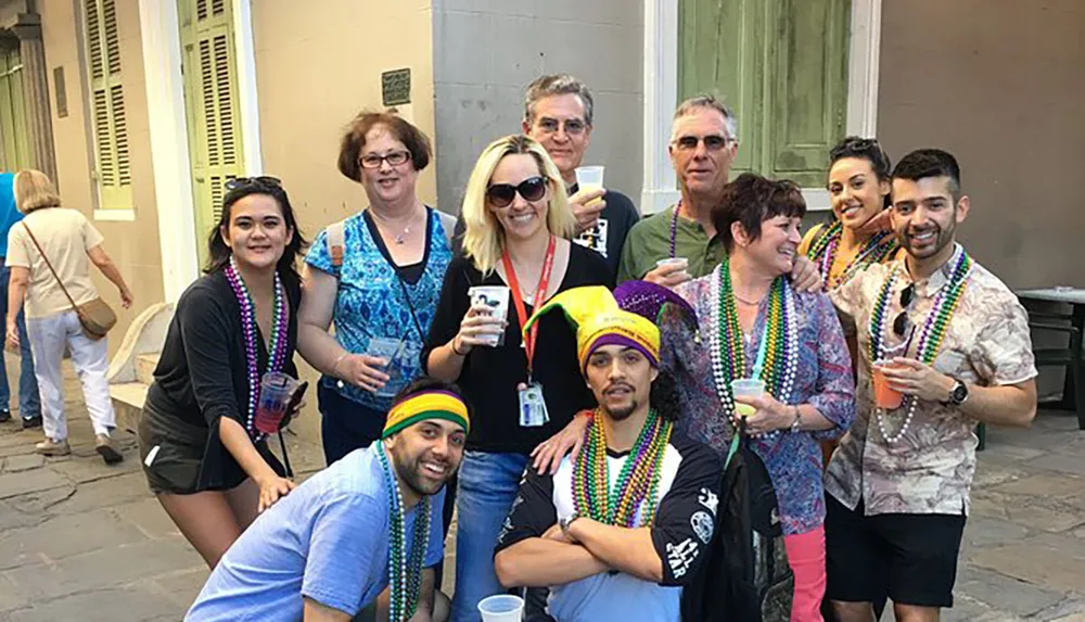 A group of people is posing for a photo while wearing colorful beads and some with festive headgear likely enjoying an outdoor event or celebration