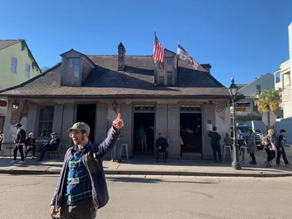 A person is cheerfully gesturing with a peace sign in front of a historic-looking building adorned with American flags under a clear blue sky