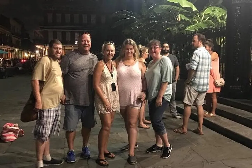 A group of people is smiling for the camera during an evening out perhaps on vacation in a lively outdoor setting with other pedestrians in the background