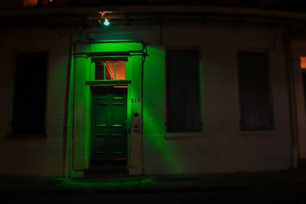The image shows an exterior view of a building entrance at night bathed in an eerie green light that casts dramatic shadows around the doorway and windows