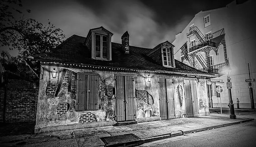 This black and white image depicts a historic-looking brick building with shutters illuminated by street lights at night providing an atmospheric and slightly eerie mood