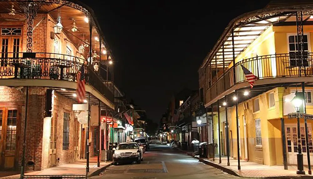 This image captures a tranquil night scene on a street lined with historic buildings featuring wrought iron balconies illuminated by streetlights in what appears to be the French Quarter of New Orleans