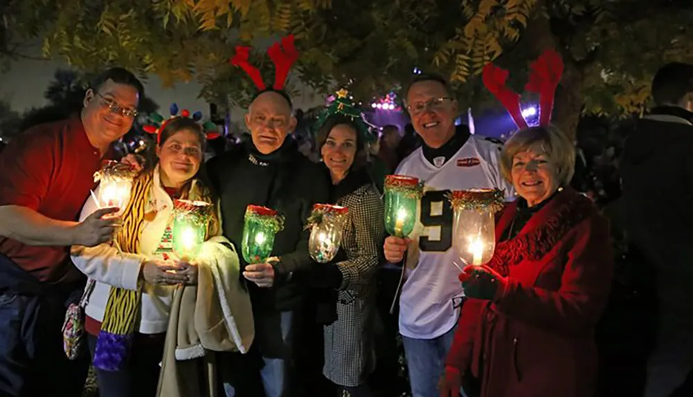 A group of people is joyfully participating in a nighttime outdoor event holding illuminated holiday-themed glasses with some wearing festive reindeer antler headbands