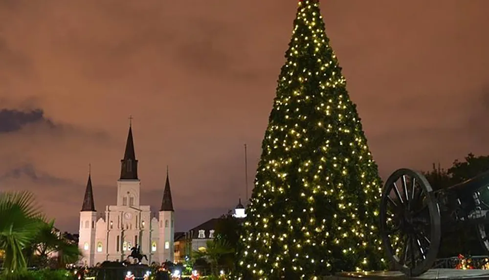 An illuminated Christmas tree stands before a historic church with a dramatic evening sky in the background