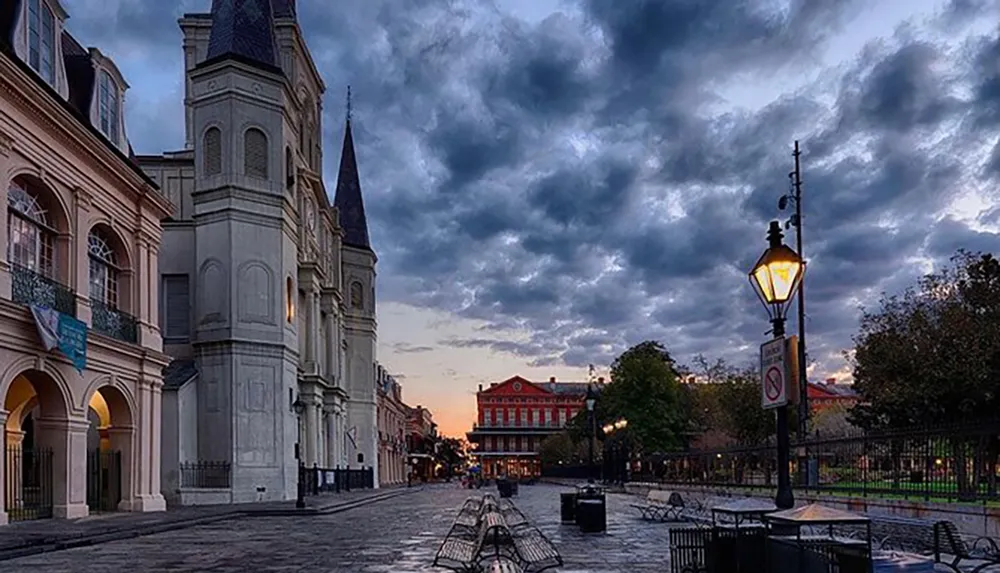 Dawn or dusk sets over a picturesque empty urban street lined with historical buildings and lamp posts under a sky heavy with dramatic clouds