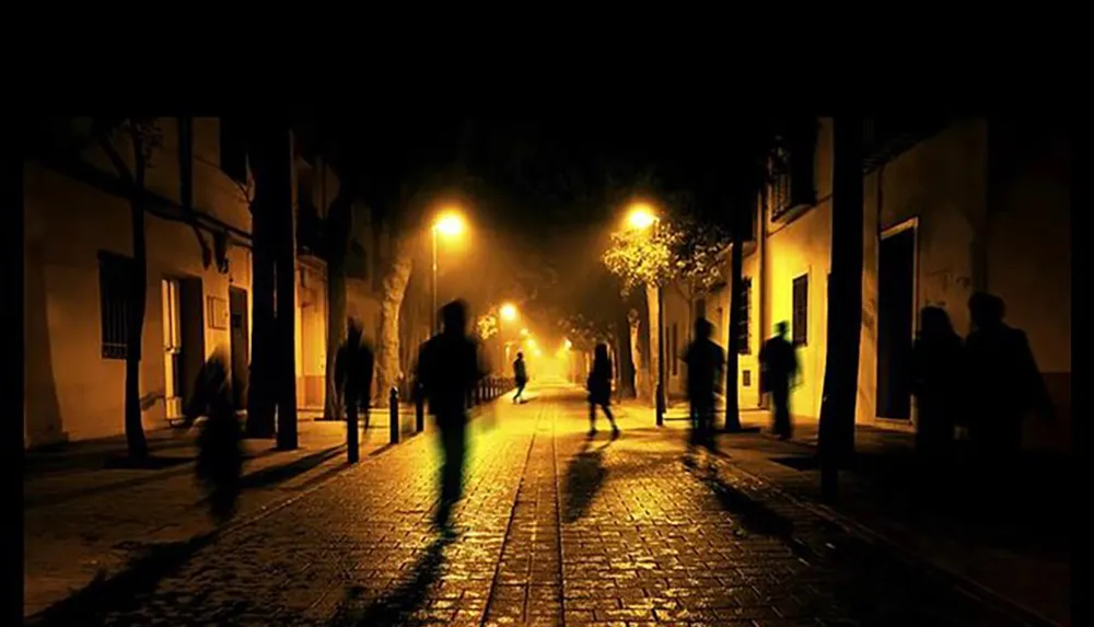 The image captures a dimly lit atmospheric cobblestone street at night with silhouetted figures of people walking and creating a moody and somewhat mysterious scene