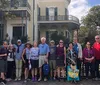 A group of tourists is posing for a photo in front of a historic house with ornate ironwork on its balcony