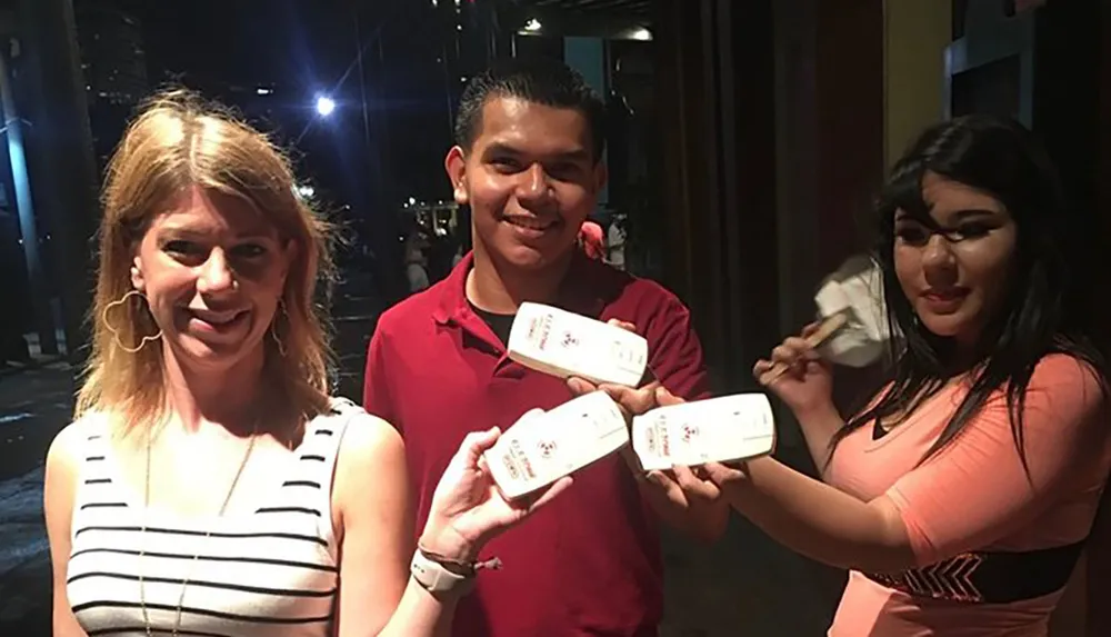 Three people are smiling and displaying their tickets or passes for an event at night time