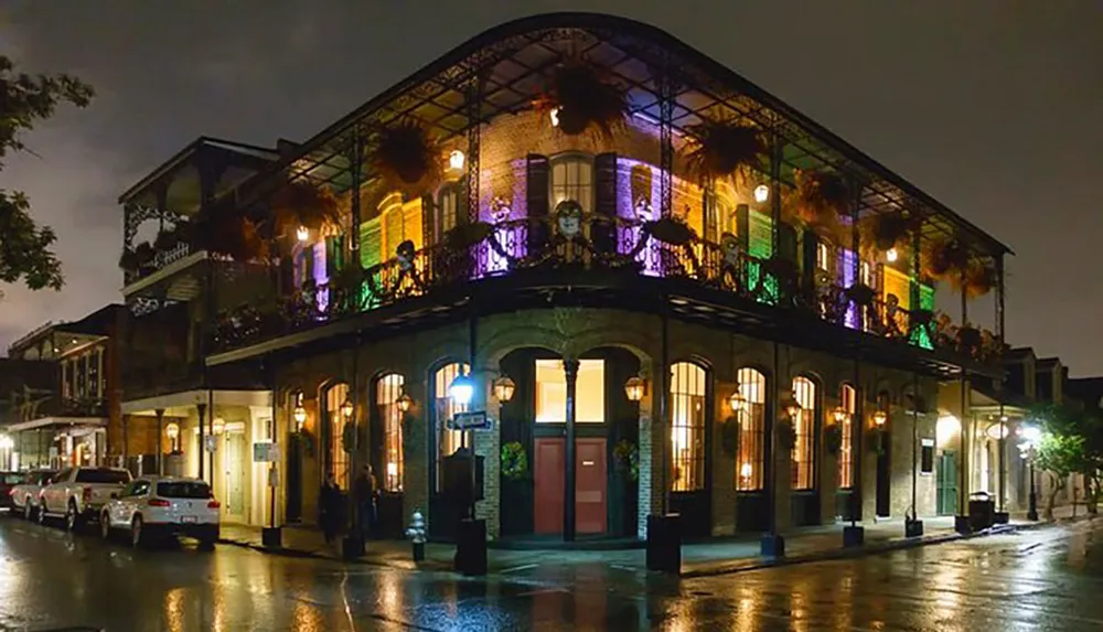 An ornate two-storey building with wrought-iron balconies is illuminated at night reflecting the distinctive architectural style of the French Quarter in New Orleans