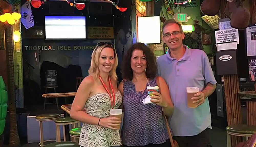 Three people are smiling for a photo inside a vibrant bar with tropical-themed decor holding drinks in their hands