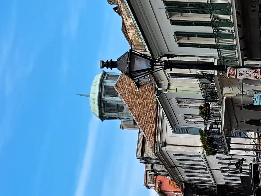 The image shows a street view of a historic building with a distinctive green cupola a black streetlamp in the foreground and a clear blue sky although the photo appears to be rotated 90 degrees to the right