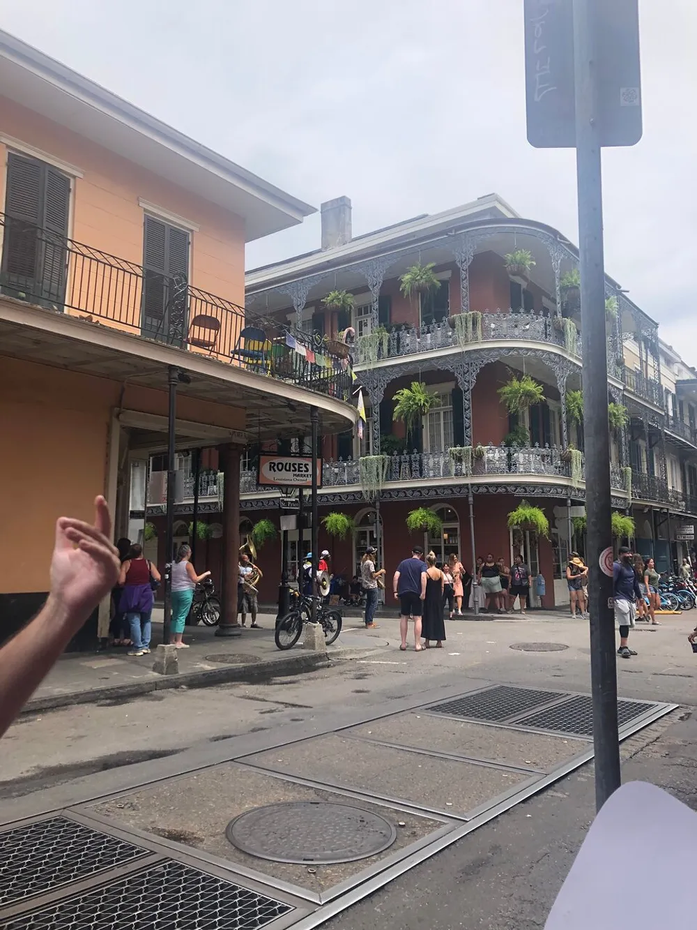 The image captures a lively street scene with people walking and classic wrought-iron balconies in what appears to be the French Quarter of New Orleans