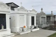 The image depicts a series of above-ground tombs and mausoleums, typical of a New Orleans cemetery, under an overcast sky.