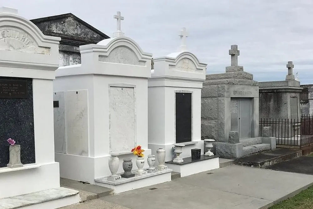The image depicts a series of above-ground tombs and mausoleums typical of a New Orleans cemetery under an overcast sky
