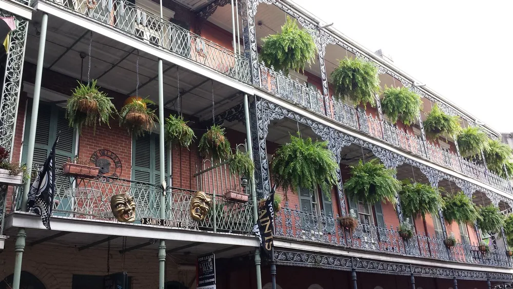 This image features a two-tiered wrought iron balcony adorned with hanging ferns on a brick building evoking the historic charm of New Orleans architecture