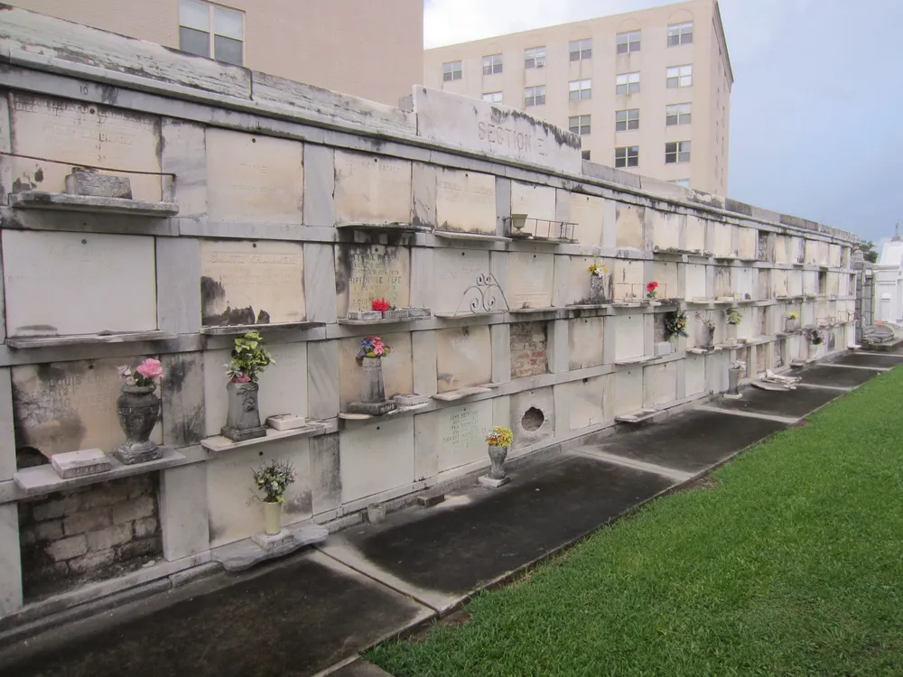 The image shows a series of above-ground tombs with floral tributes a typical sight in a New Orleans cemetery under an overcast sky