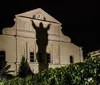 The image depicts a shadowy figure with arms raised projected onto the faade of a building that resembles a church creating a haunting and dramatic effect at night