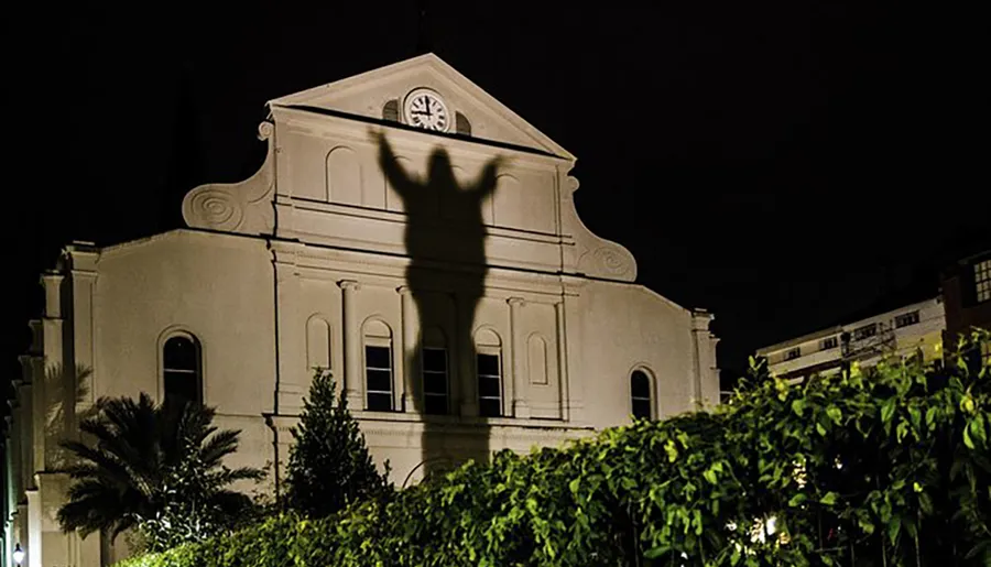 The image depicts a shadowy figure with arms raised, projected onto the façade of a building that resembles a church, creating a haunting and dramatic effect at night.