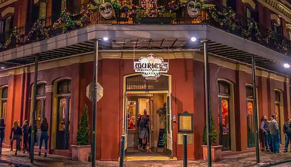 The image shows a vibrant entrance to a place called Tujagues a restaurant or bar adorned with Mardi Gras masks on the balcony above creating a festive New Orleans atmosphere as people walk by on the sidewalk