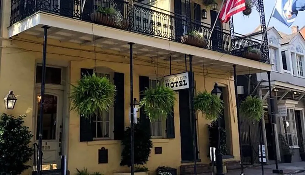 The image shows the exterior of a charming two-story building with a balcony housing a hotel adorned with plants and flags capturing the essence of a picturesque urban setting