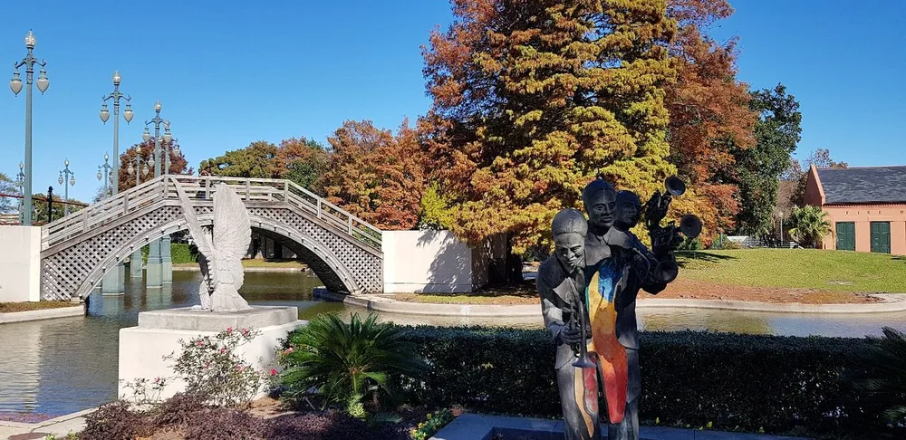 A statue of a Jazz band is in the foreground with a picturesque arched bridge and autumn-colored trees in the background